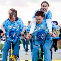 Students riding two tricycles while wearing matching tie-die Lakerpalooza shirts